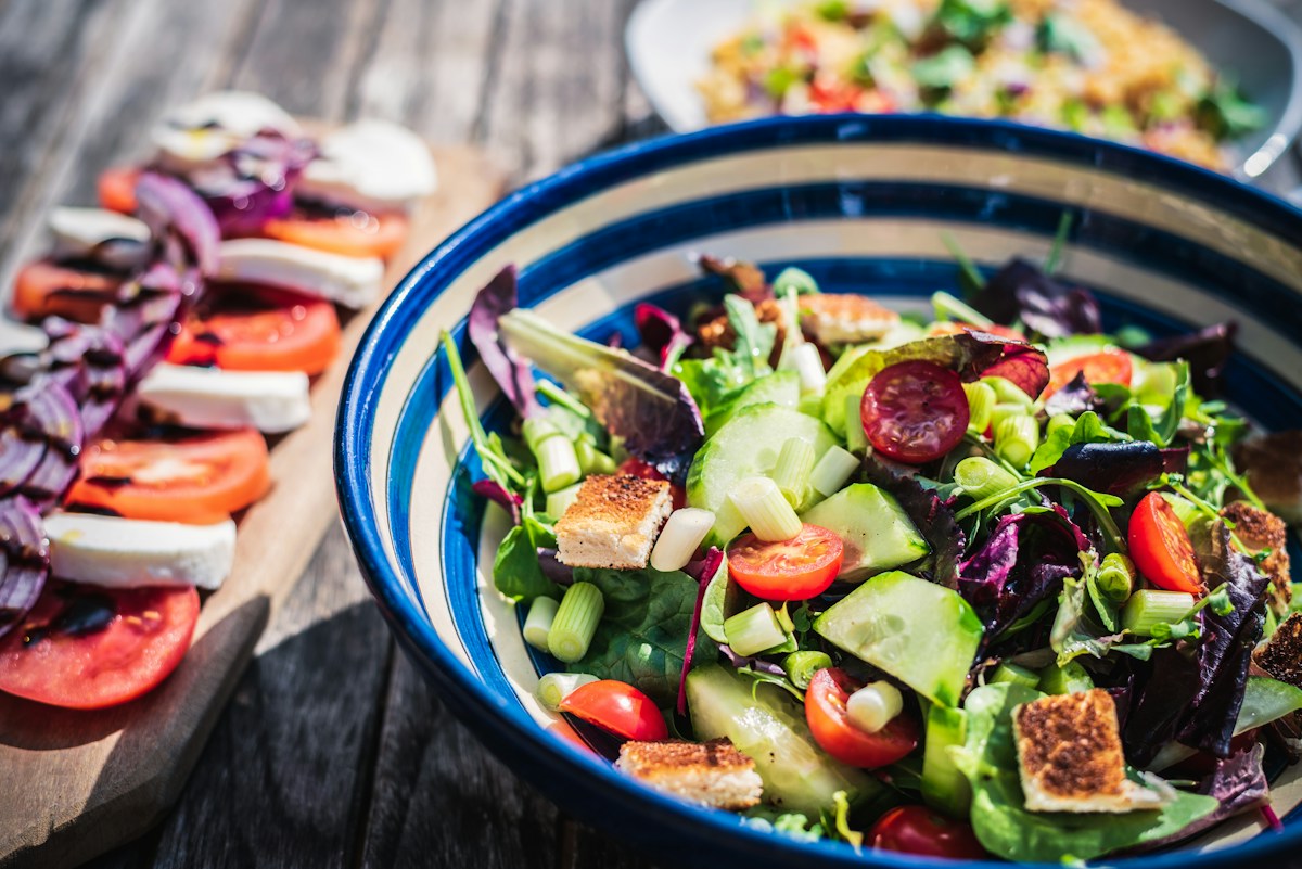 A colourful salad in a blue bowl beside sliced tomatoes and cheese