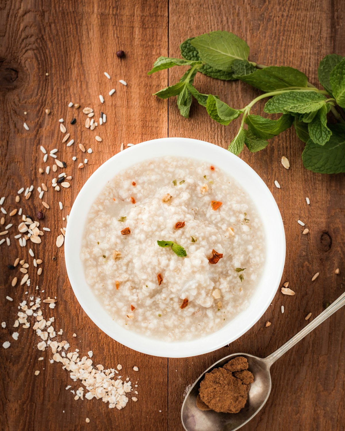 A bowl of oatmeal on a wooden table with scattered oats