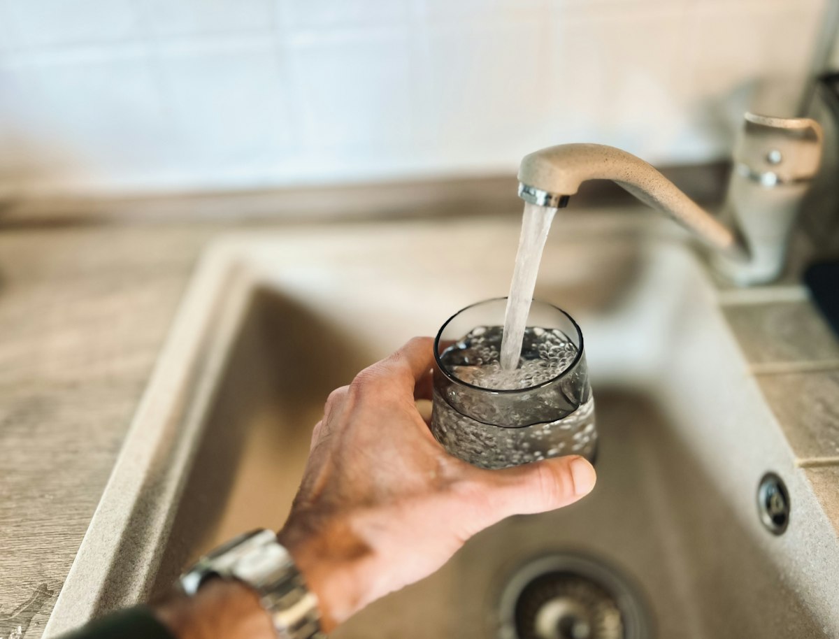 A hand holding a clear glass of drinking water