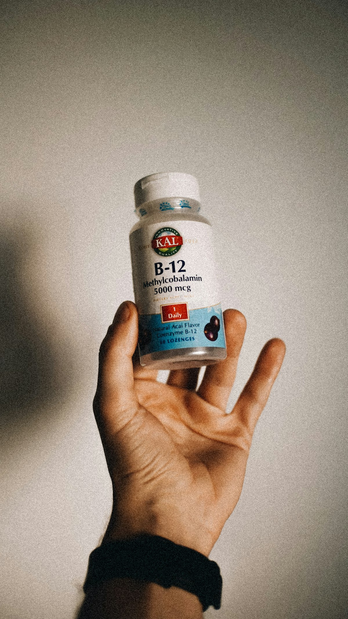 A hand holding a labelled vitamin B12 supplement bottle